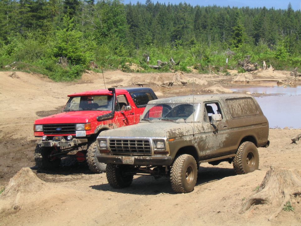Mud-covered 1978 Ford Bronco parked on dirt with a red Ford Bronco behind it
