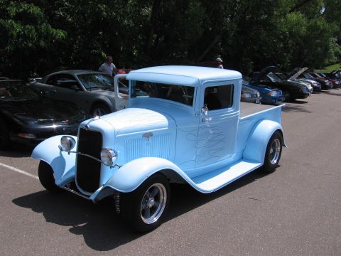 1989 Ford Mustang - A light blue hot rod pickup truck with flame decals is parked at an outdoor car show.