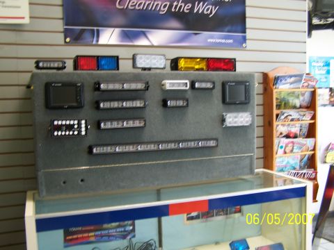 2003 Ford Crown Victoria - A collection of emergency vehicle lighting options are displayed on a gray board against a striped wall.