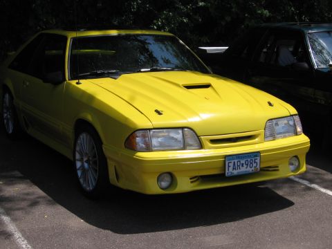 1989 Ford Mustang - Yellow 1989 Ford Mustang with a hood scoop and aftermarket wheels.
