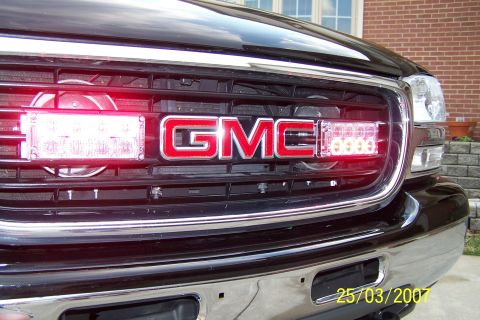 2003 Ford Crown Victoria - The front grille of a GMC truck is illuminated by red LED light bars flanking the emblem.