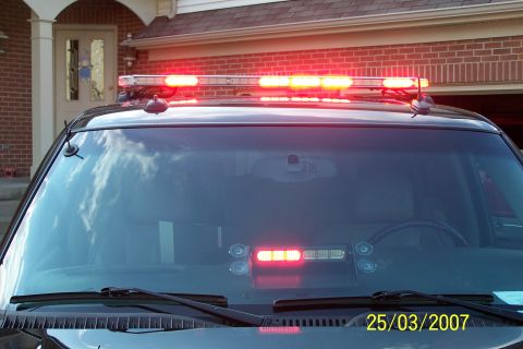 2003 Ford Crown Victoria - A police car is shown from the front, a light bar on the roof and red lights activated on the dashboard.