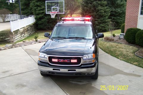 2003 Ford Crown Victoria - This GMC SUV has emergency lights mounted on the roof and grille, suggesting it might be a police or emergency vehicle.