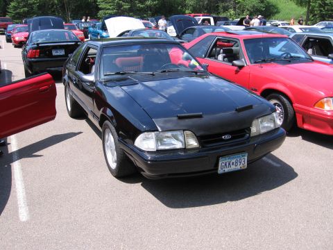 1989 Ford Mustang - A black Ford Mustang is parked at a car show with other vehicles around it.