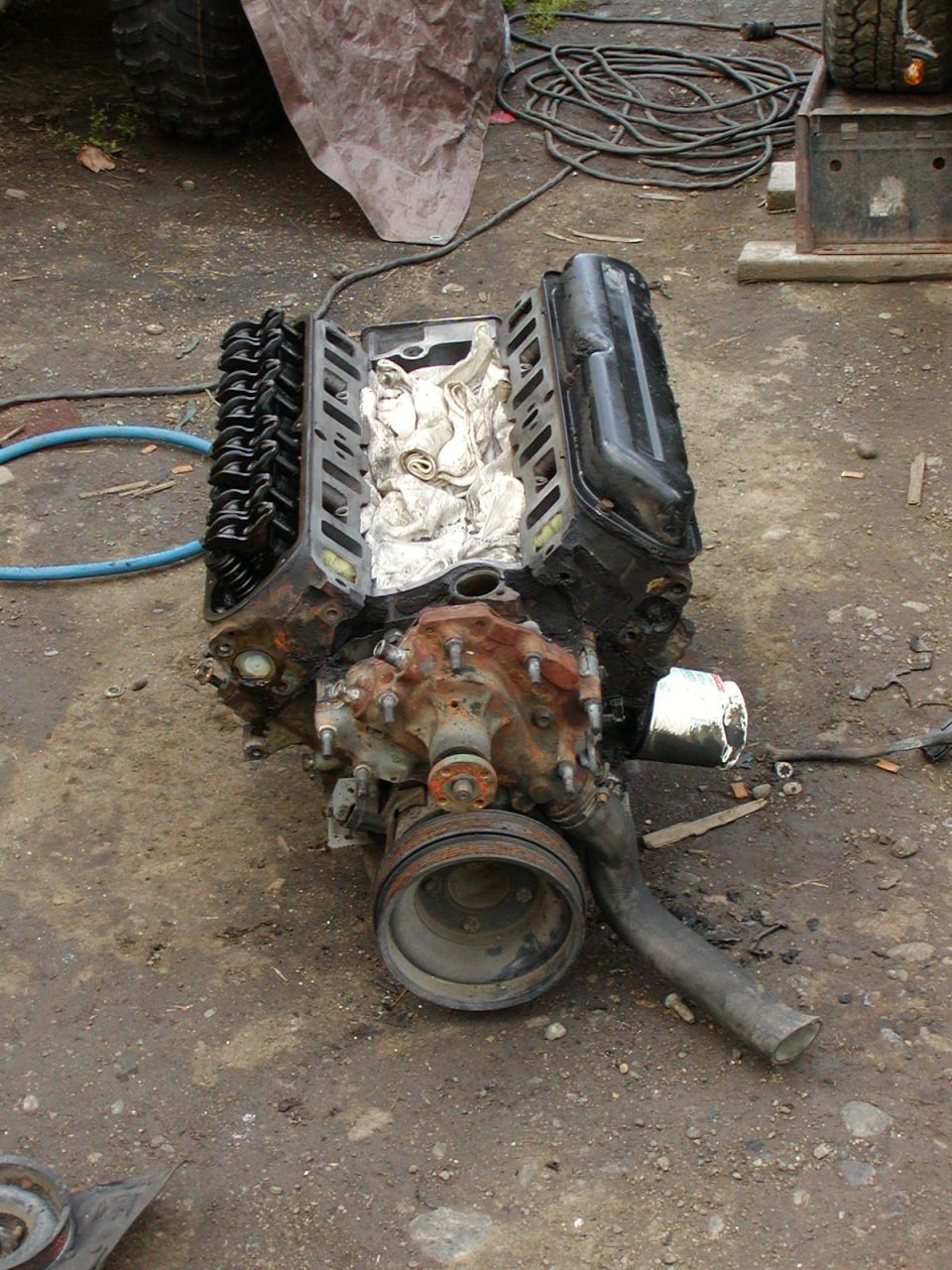 Removed V8 engine on the ground with valve cover off, rags in valley, water pump and pulley visible at front