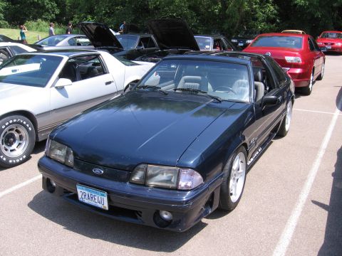 1989 Ford Mustang - A dark blue 1989 Ford Mustang is parked in a lot with other vehicles, some with hoods open.
