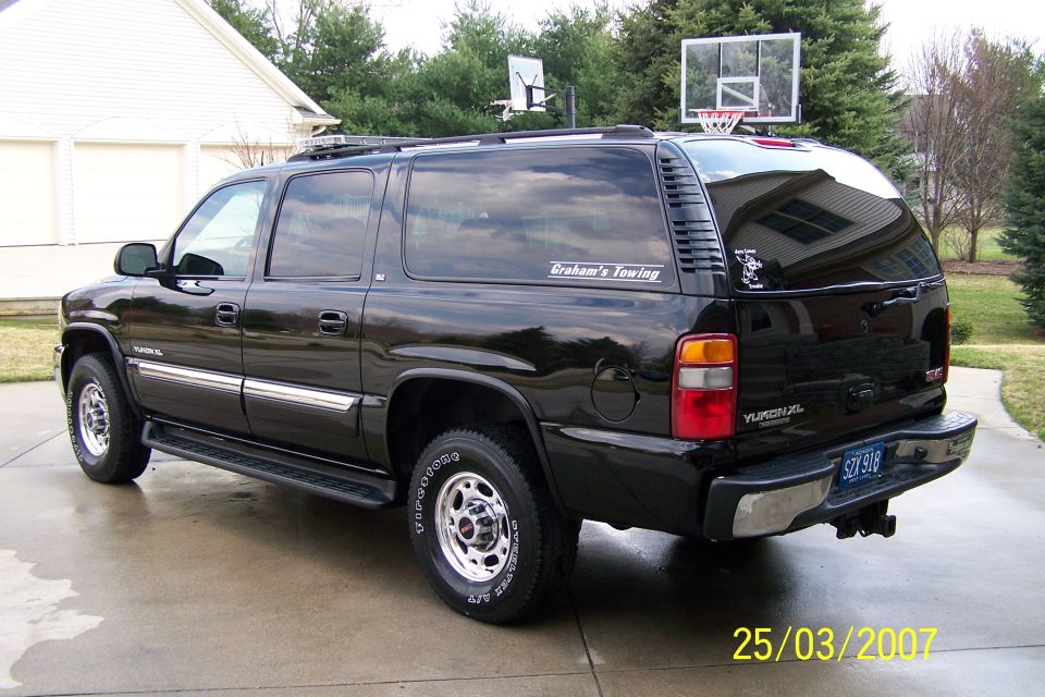 Black GMC Yukon XL SUV with chrome trim and running boards, parked on a wet driveway