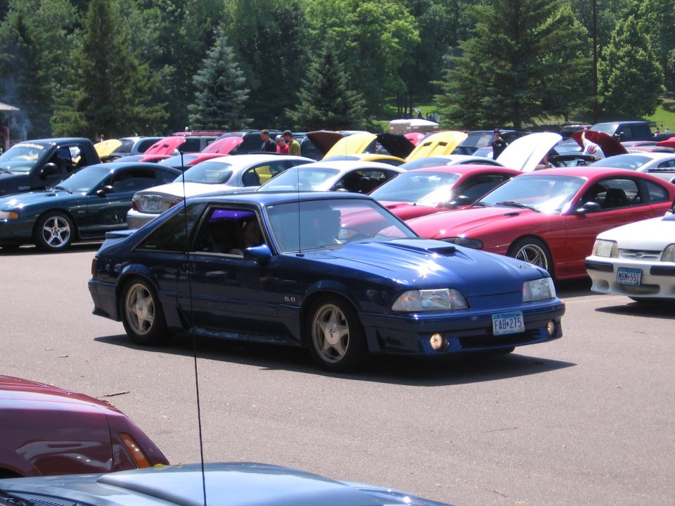 Blue 1989 Ford Mustang with a hood scoop and 5.0 badge, parked in a lot with other cars