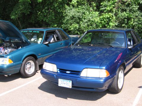 1989 Ford Mustang - Two Ford Mustangs, a blue one in front and a teal one behind it, are parked at an outdoor event.