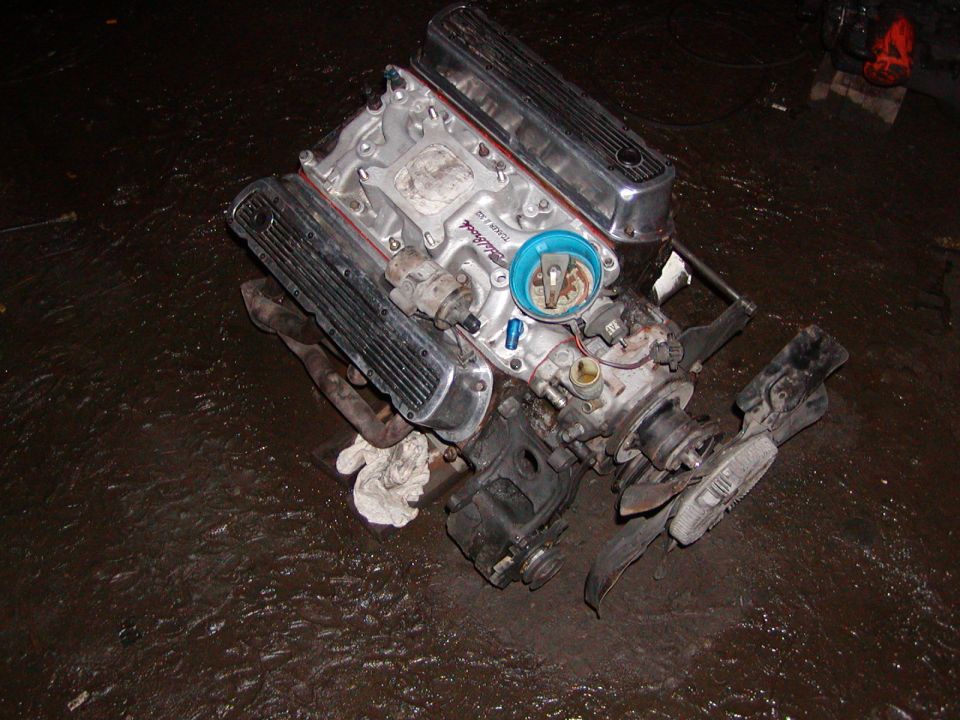 Removed V8 engine with chrome valve covers, Edelbrock intake, and fan sitting on a garage floor