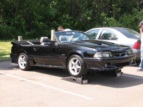 1989 Ford Mustang - A black convertible Mustang is parked on ramps, with another car visible behind it.