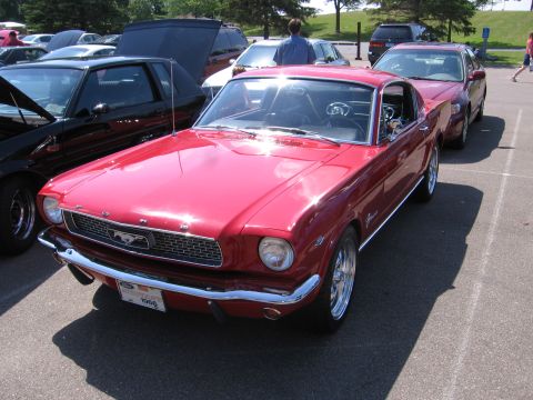 1989 Ford Mustang - This red classic Ford Mustang is parked in a lot, with other vehicles visible in the background.