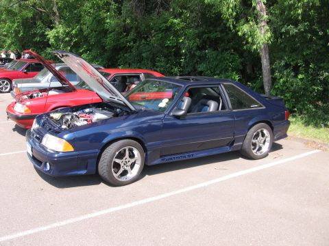 1989 Ford Mustang - A dark blue 1989 Ford Mustang GT is parked with its hood open, alongside other vehicles at an outdoor gathering.