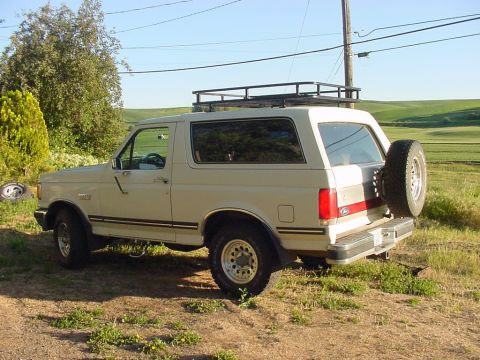 Tan 1988 Ford Bronco with roof rack and rear spare tire, seen from 3/4 front