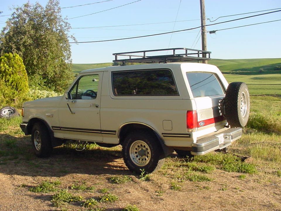 Tan 1988 Ford Bronco with roof rack and rear spare tire, seen from 3/4 front