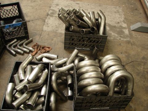 1992 Ford Taurus - Various metal exhaust pipes are organized in black crates on a workshop floor.