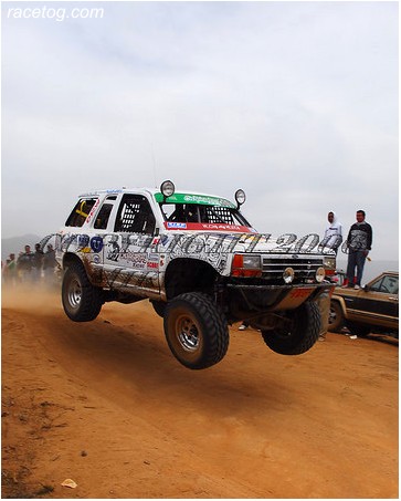 1992 Ford Explorer - This modified SUV is airborne during a race, kicking up dust on a dirt track.