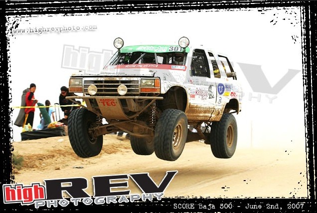 White off-road truck mid-air, front grille visible, modified suspension, racing decals