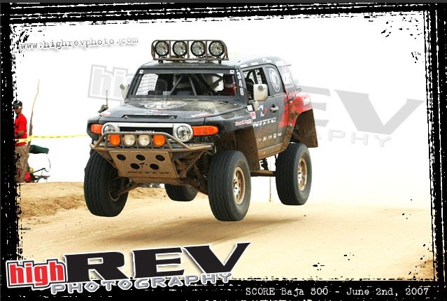 Black off-road SUV with roof lights and front bumper guard airborne over sand