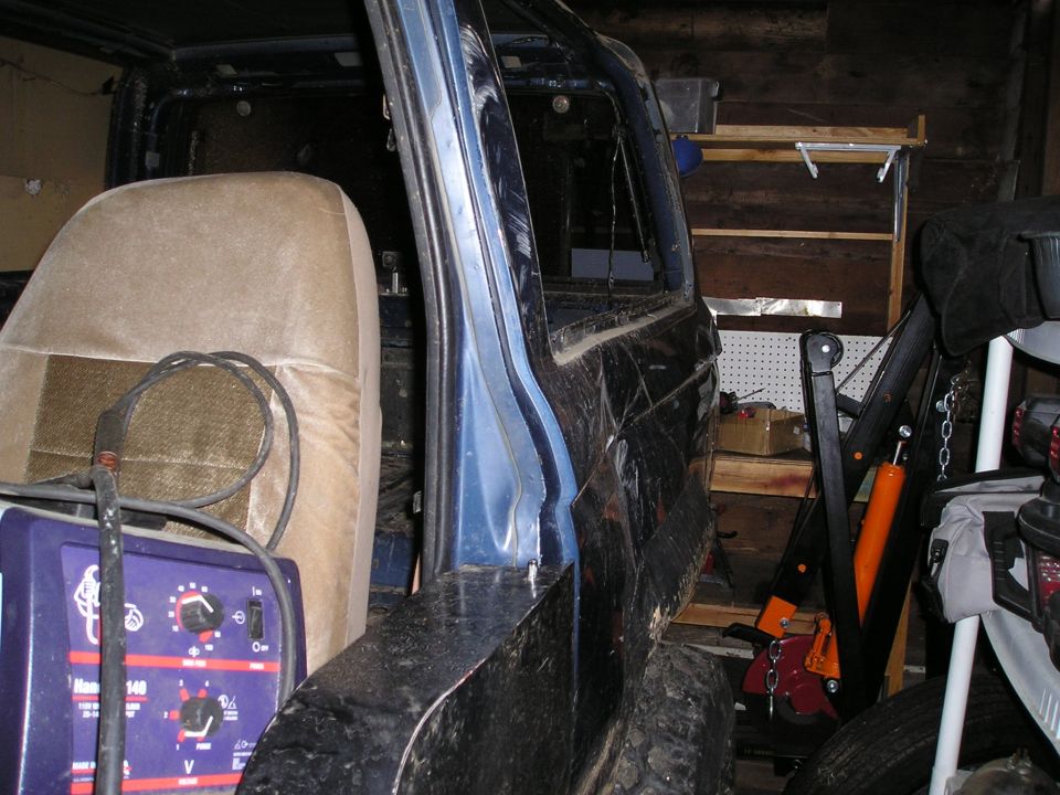 Interior view of a vehicle with a welding machine and a hoist nearby. The vehicle appears to be undergoing repairs