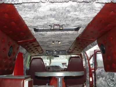 1978 Ford E250 - The interior of a van features custom carpeting and padded walls, with a table and seats visible.