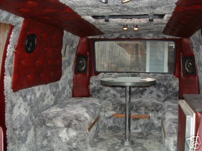 1978 Ford E250 - The interior of a van is customized with plush grey carpeting and red padded walls, complete with a table and speakers.