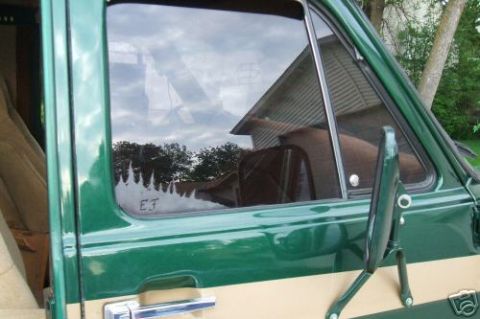 1978 Ford E250 - Reflection in the side window of a green van shows trees and a house. EJ is etched on the glass.