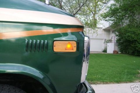 1978 Ford E250 - Close-up of a green van's front fender, showing decorative wood trim and an amber turn signal light.