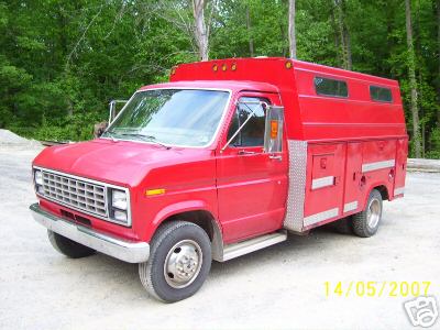 1978 Ford E250 - This 1978 Ford E250 utility truck features a custom camper shell and toolboxes, seen in a wooded area.