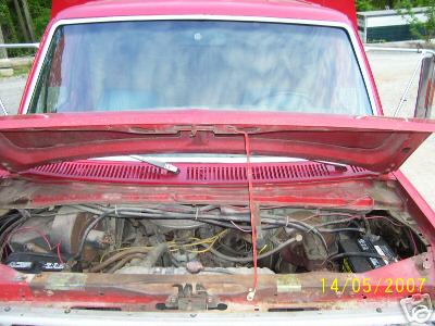 1978 Ford E250 - The engine bay of a red Ford van, revealing its mechanical components and two batteries.
