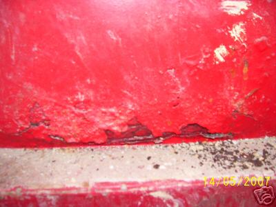 1978 Ford E250 - The lower section of a red panel shows significant rust and deterioration, with a concrete surface below.