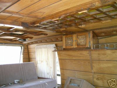 1978 Ford E250 - The interior of a van shows wood paneling, a couch, and cabinets, with visible damage to the ceiling panels.
