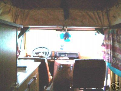 1978 Ford E250 - The interior of a van shows the dashboard, steering wheel, and seats, with curtains on the side.