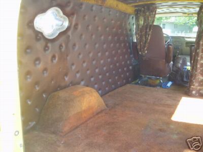 1978 Ford E250 - Interior of a custom van cargo area looking forward from the open rear doors, with brown tufted button upholstery on the side wall, a scall…