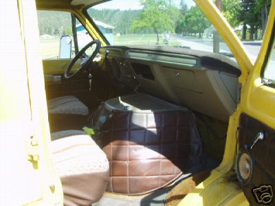 1978 Ford E250 - Interior of a yellow van shot from the side doorway looking across the cab, showing the black doghouse engine cover between brown vinyl sea…