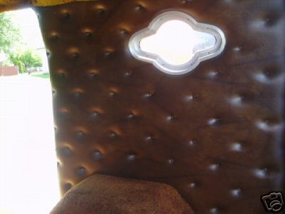 1978 Ford E250 - Close-up of a custom van interior side panel finished in brown tufted button-studded vinyl, with a chrome-bezeled quatrefoil-shaped porthol…