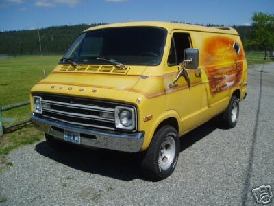 1978 Ford E250 - Yellow 1970s Dodge shorty van shot from the front three-quarter angle on pavement, with green fields and pine-covered hills behind it. It w…