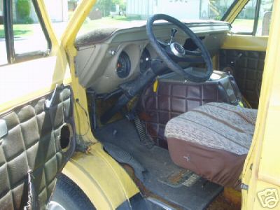 1978 Ford E250 - Interior of a yellow van shot through the open driver's door, showing a brown bucket seat, tan dash with round gauge pods, a black three-sp…