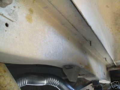 1978 Ford E250 - Close-up underbody shot looking along a van's frame rail and rocker area, showing surface rust staining and undercoating on white-painted s…