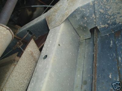 1978 Ford E250 - Tight close-up of weathered gray sheet-metal body panels and a bracket, showing surface pitting, dirt and a drilled hole where pieces overl…