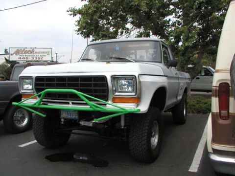 1979 Ford Bronco - A silver 1979 Ford Bronco is parked in a lot, a prominent green bull bar and off-road tires.