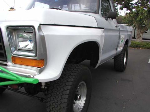 1979 Ford Bronco - The front fender and headlight of a 1979 Ford Bronco are visible, a green bumper and a decal on the door.