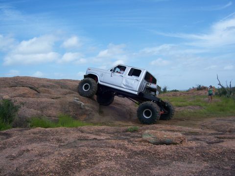 1979 Ford Bronco - A heavily modified truck navigates a challenging rocky terrain under a partly cloudy sky.