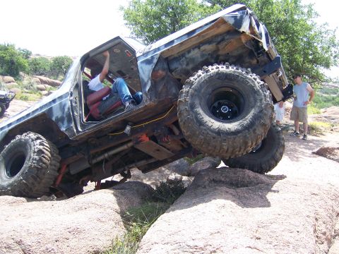 1979 Ford Bronco - An off-road vehicle navigates a rocky terrain, with its driver inside and large tires gripping the stones.