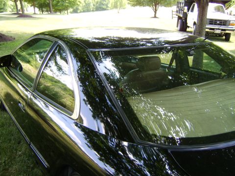 1996 Mercury Grand Marquis - Close-up rear three-quarter view of a black sedan's roof, rear window, and C-pillar, showing reflections of trees in the glossy paint and g…