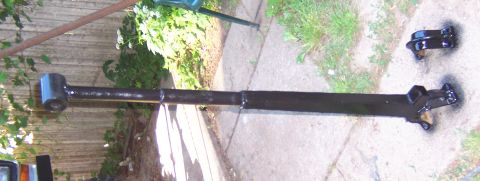 1978 Ford Bronco - A painted vehicle axle and a separate bracket sit on the ground next to a fence.