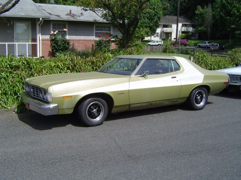 1973 Ford Torino - A two-tone coupe sits parked on a residential street next to a house and some bushes.