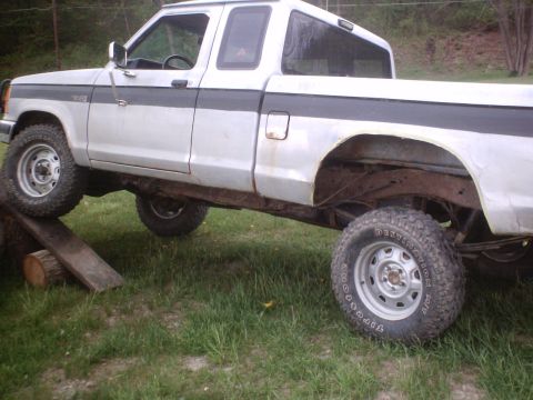 1990 Ford Ranger - This pickup truck is on a ramp made of logs and wood, with its front tire elevated.