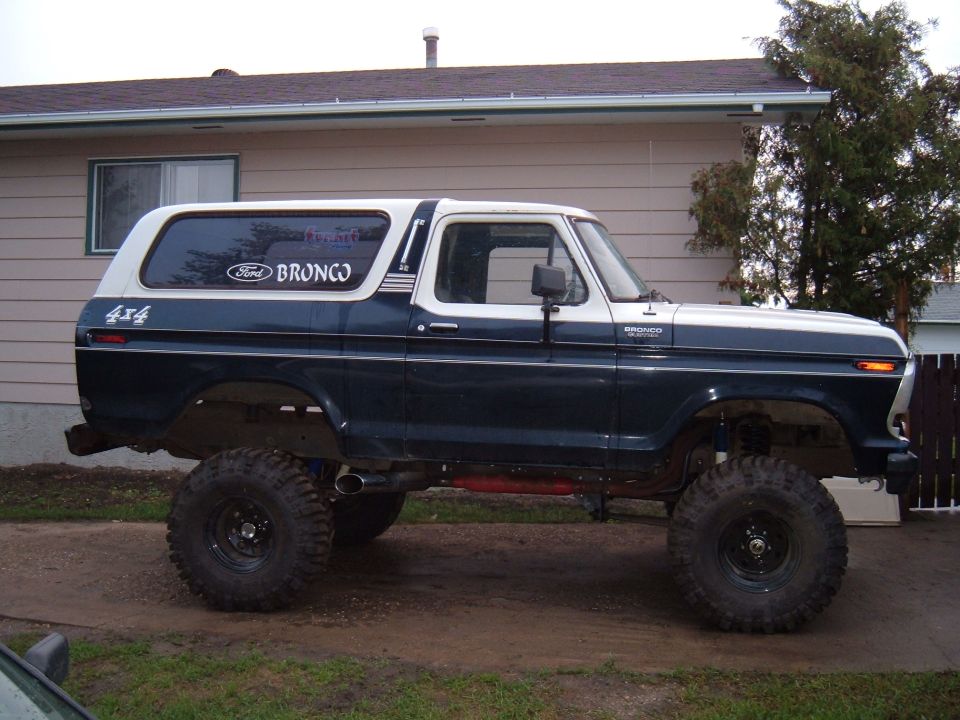 Lifted 1979 Ford Bronco, dark blue with white top, large off-road tires, parked in front of a house