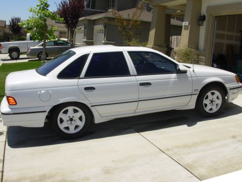 1995 Ford Taurus - A white sedan is parked in a driveway with a house and garage in the background.
